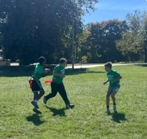 Three students running on a grassy field playing flag football.