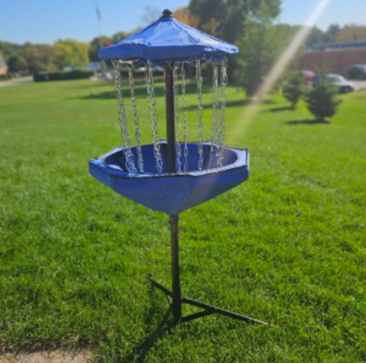 A disk golf basket out in a grassy field.