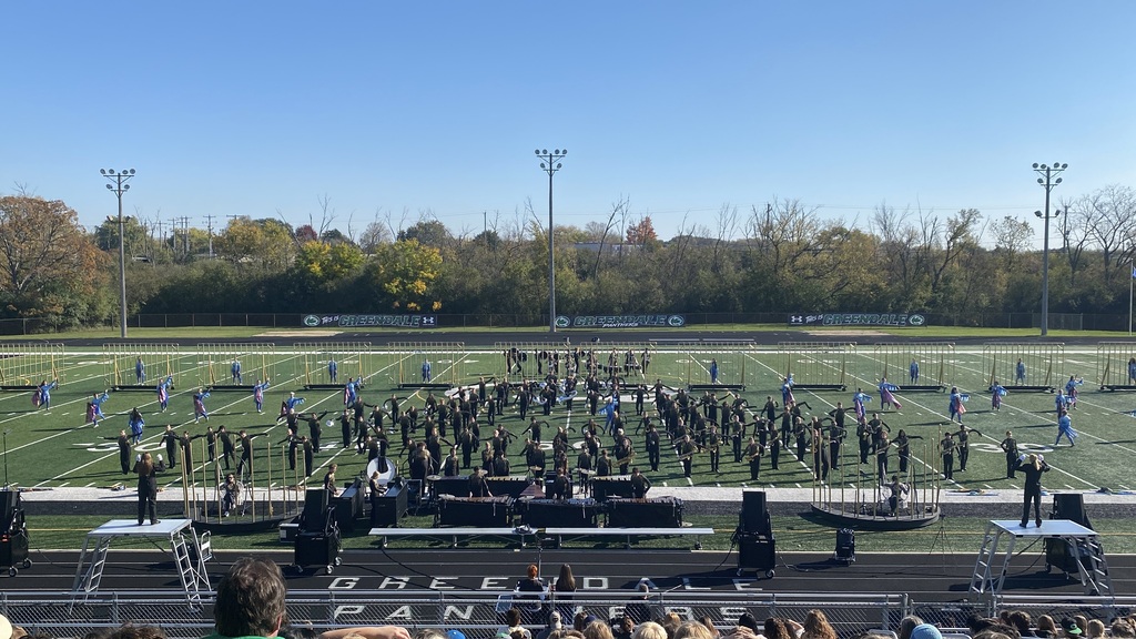 Marching band standing on a stadium field prepared to perform.