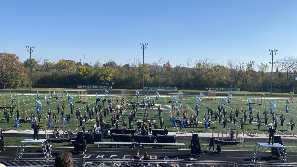 Marching band standing on a stadium field prepared to perform.