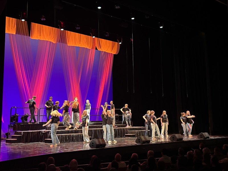Performers on stage with vibrant purple and orange lighting.