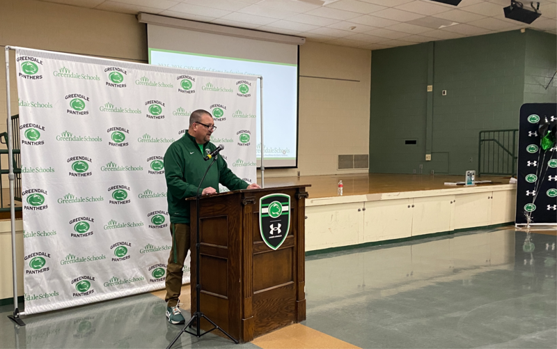 Person standing behind a podium with a white backstop behind them. They are reading a speech.