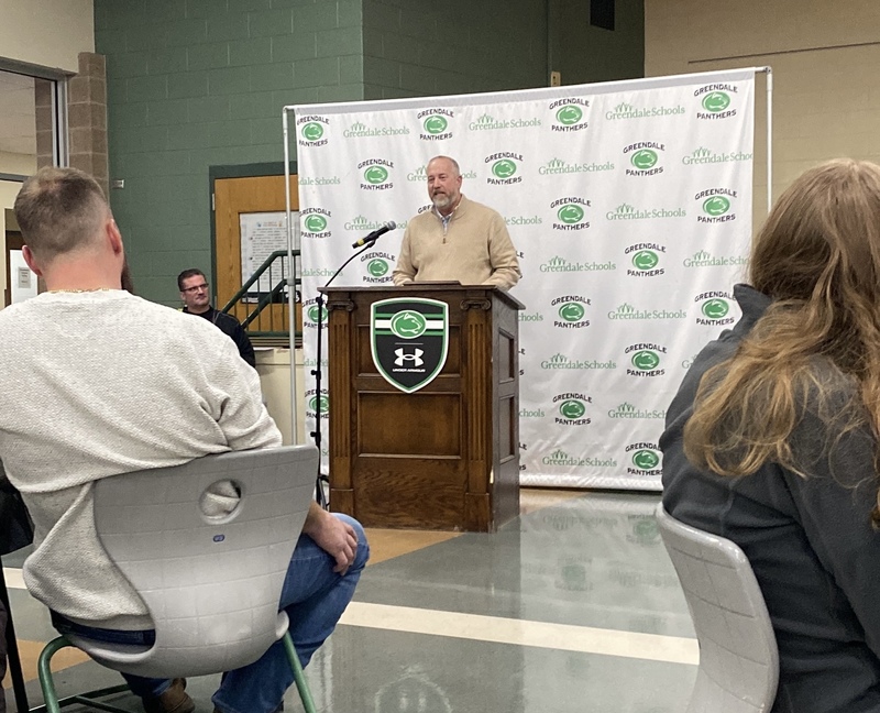Person standing behind a podium with a white backstop behind them. They are reading a speech.
