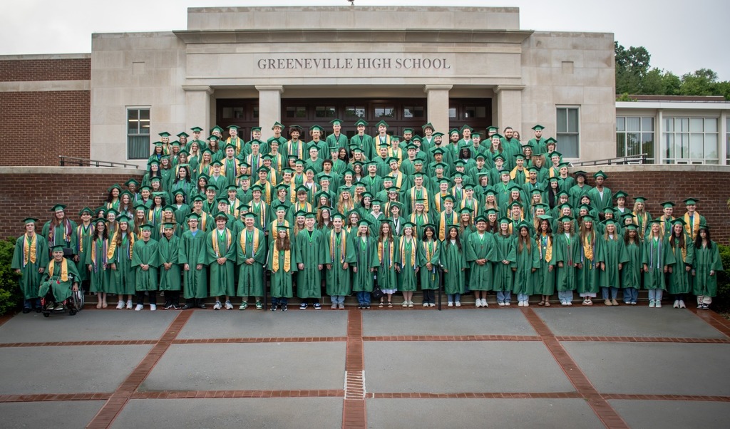 "A large group of students in green graduation gowns and caps pose on the steps of Greeneville High School. They are arranged in multiple rows, with some seated and others standing, in front of the school's entrance."