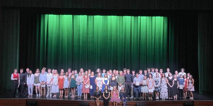 a large group of students standing on a stage in front of a green curtain backdrop