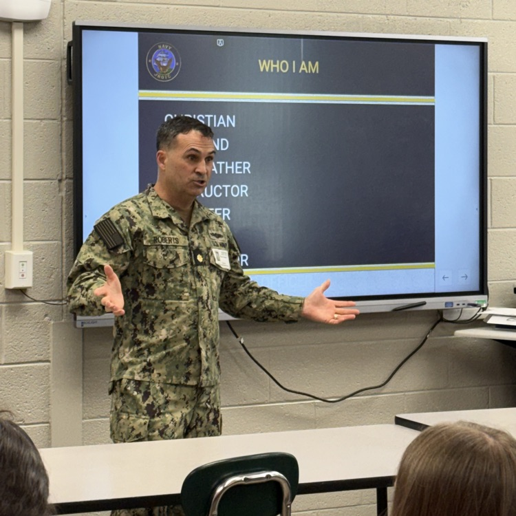 a man in a camp soldiers uniform talks to a room of students  