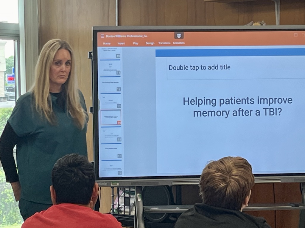 Presenter discussing patient care and memory recovery using a classroom slideshow.