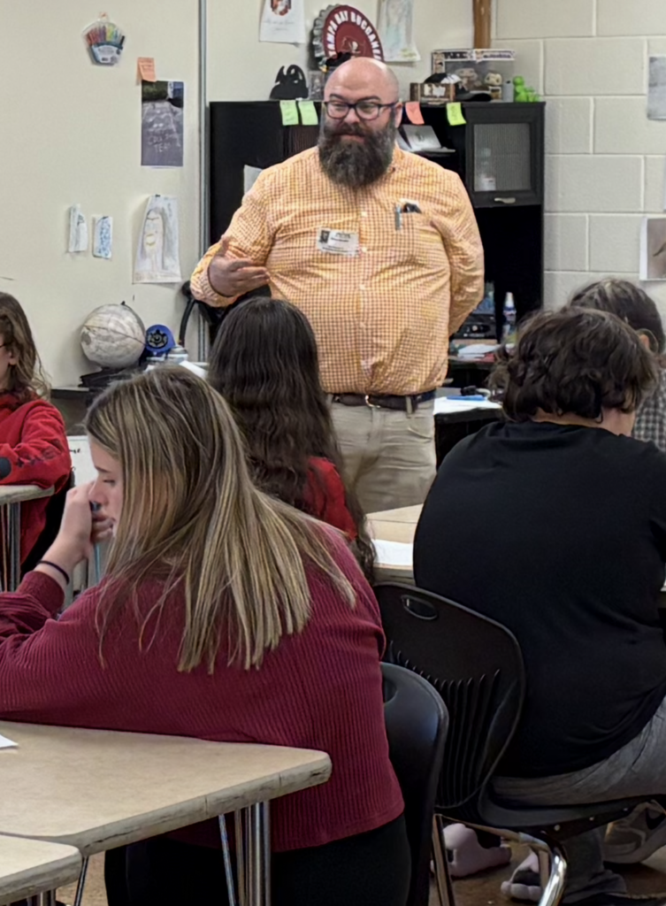 Guest speaker talking to students seated at desks during a classroom session.