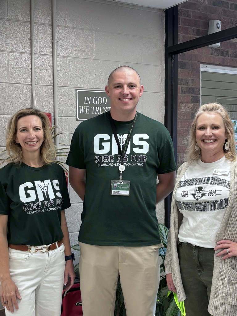 three people stand in a row smiling. they are all wearing t-shirts that say GMS, rise as one