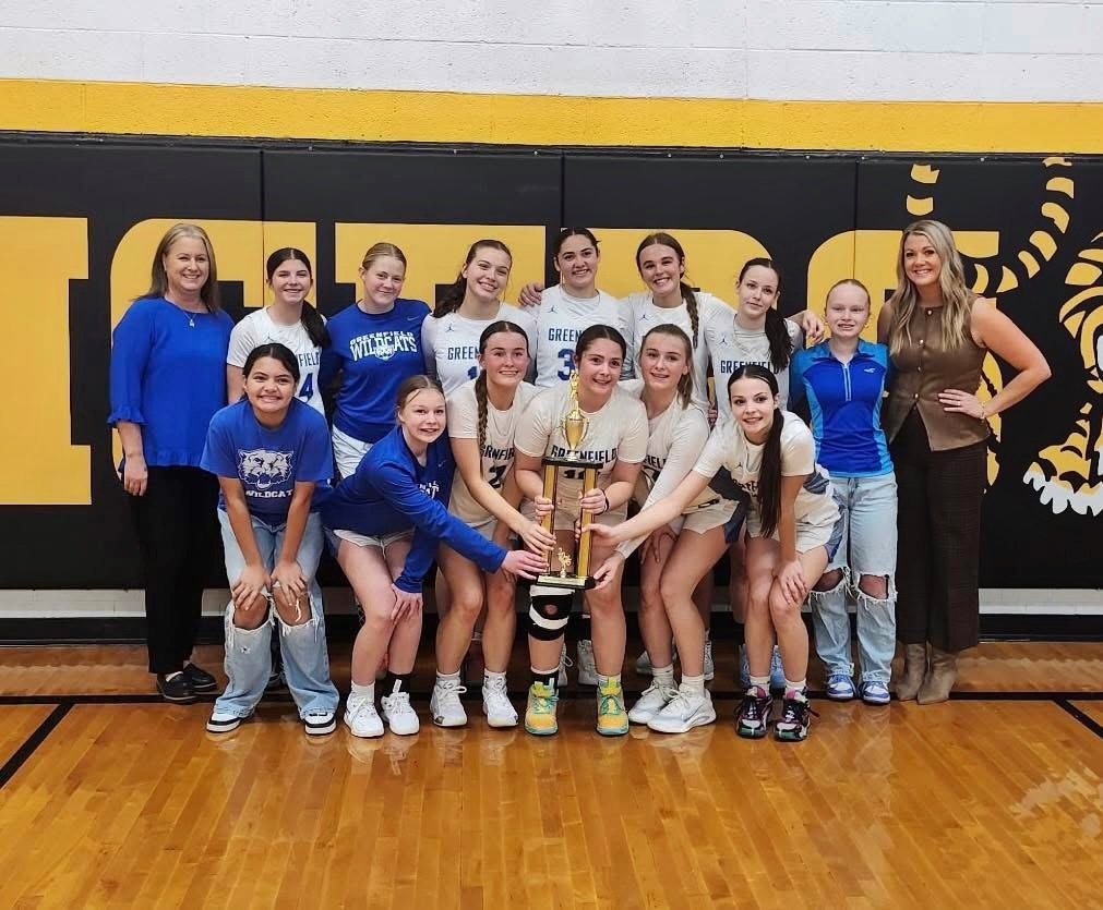 image of the Greenfield Lady Wildcats team holding the tournament trophy, with both coaches on either side of them