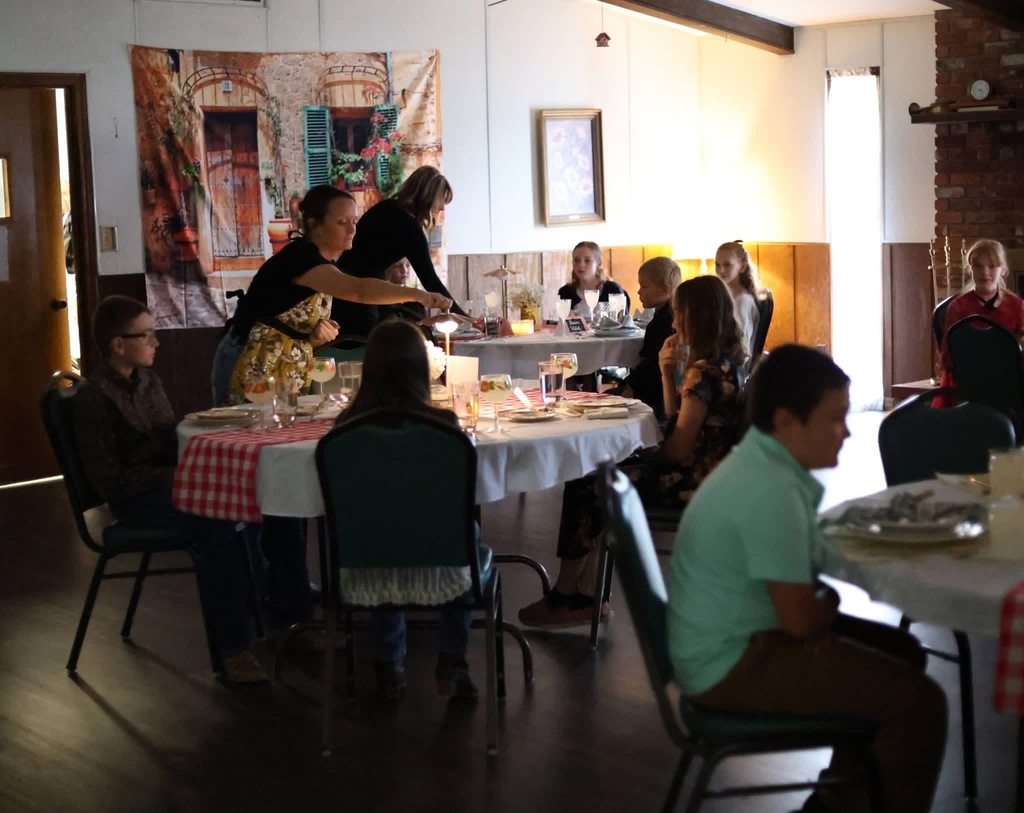 Image of several tables of 5th graders being served their meal by parent and teacher volunteers