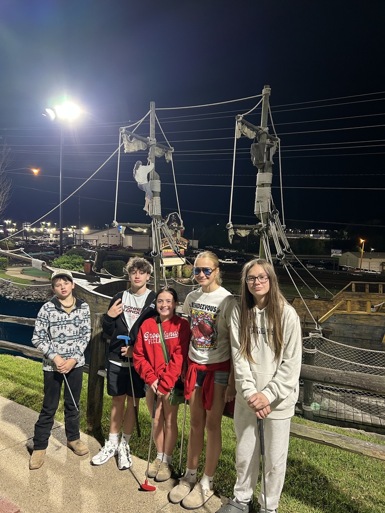 five students posing with putters in front of a pirate ship