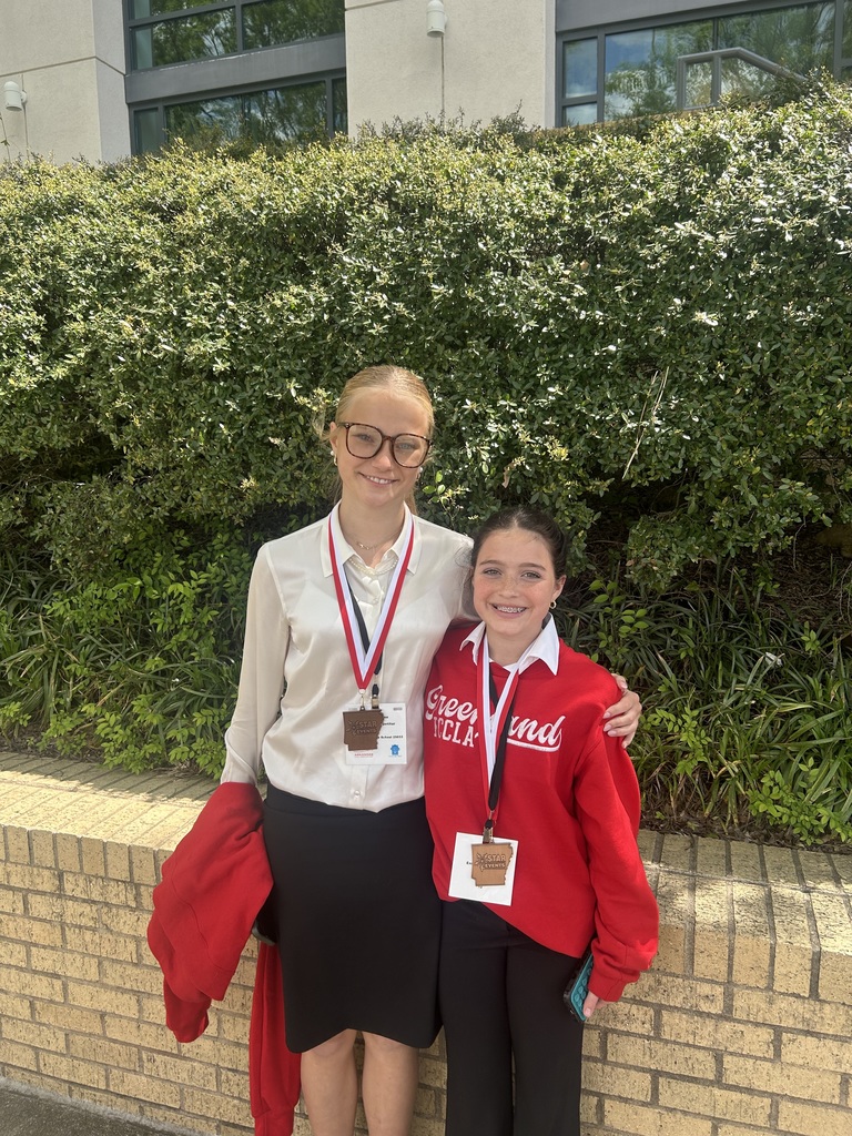 two students posing in front of greenery outside