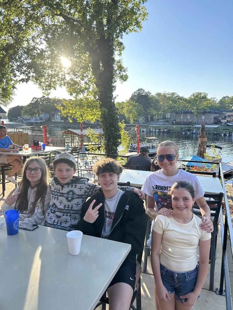 five students posing at a table with a lake in the background