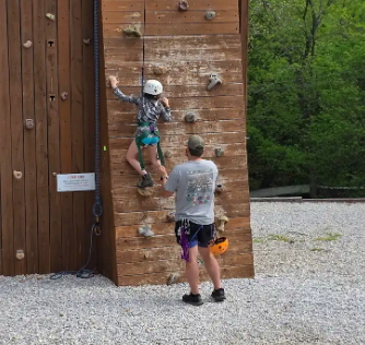 student on a rock climbing wall with an adult standing close by