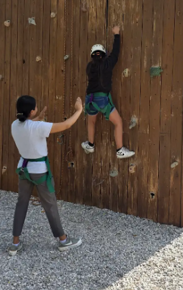 student on a rock climbing wall with an adult standing close by