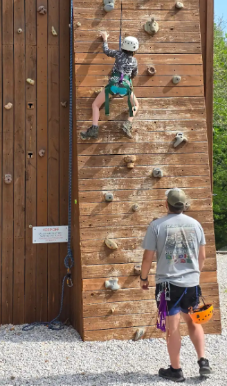 student on a rock climbing wall with an adult standing close by