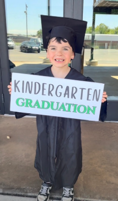 student in cap and gown holding kindergarten graduation sign