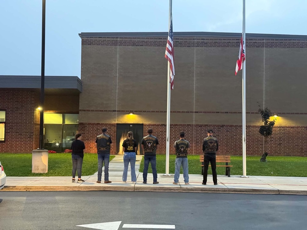 Military group standing in front of flagpoles 