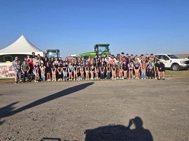 large group of students standing in front of tractors