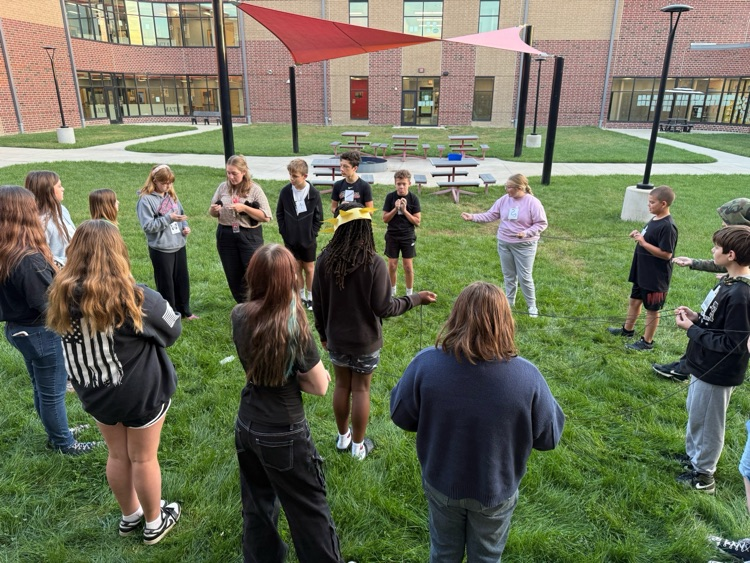 students in a circle hold yarn
