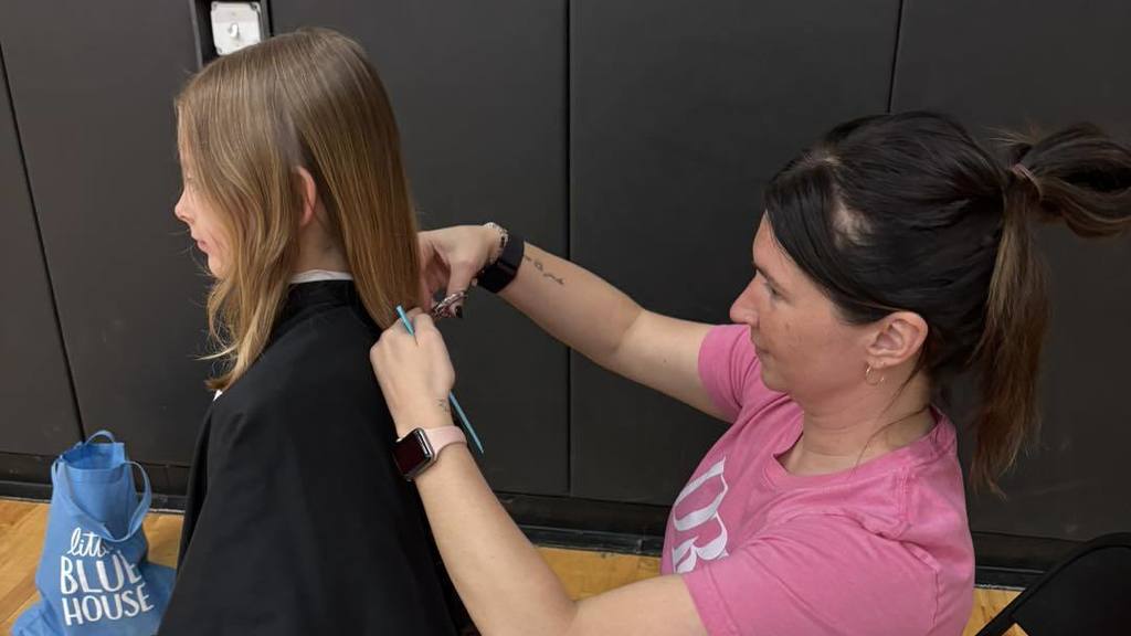 Woman with ponytail pins a student's badge on her jacket in a room with black walls.