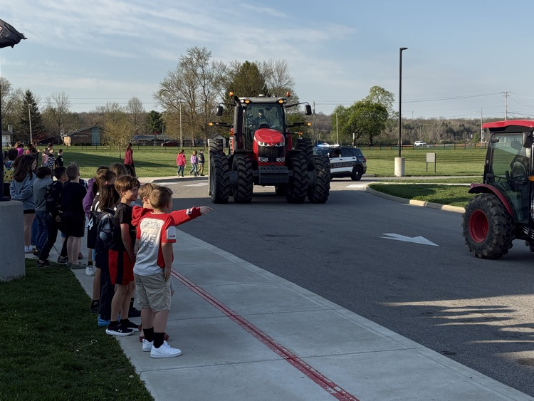 tractors driving by group of students standing on curb outside