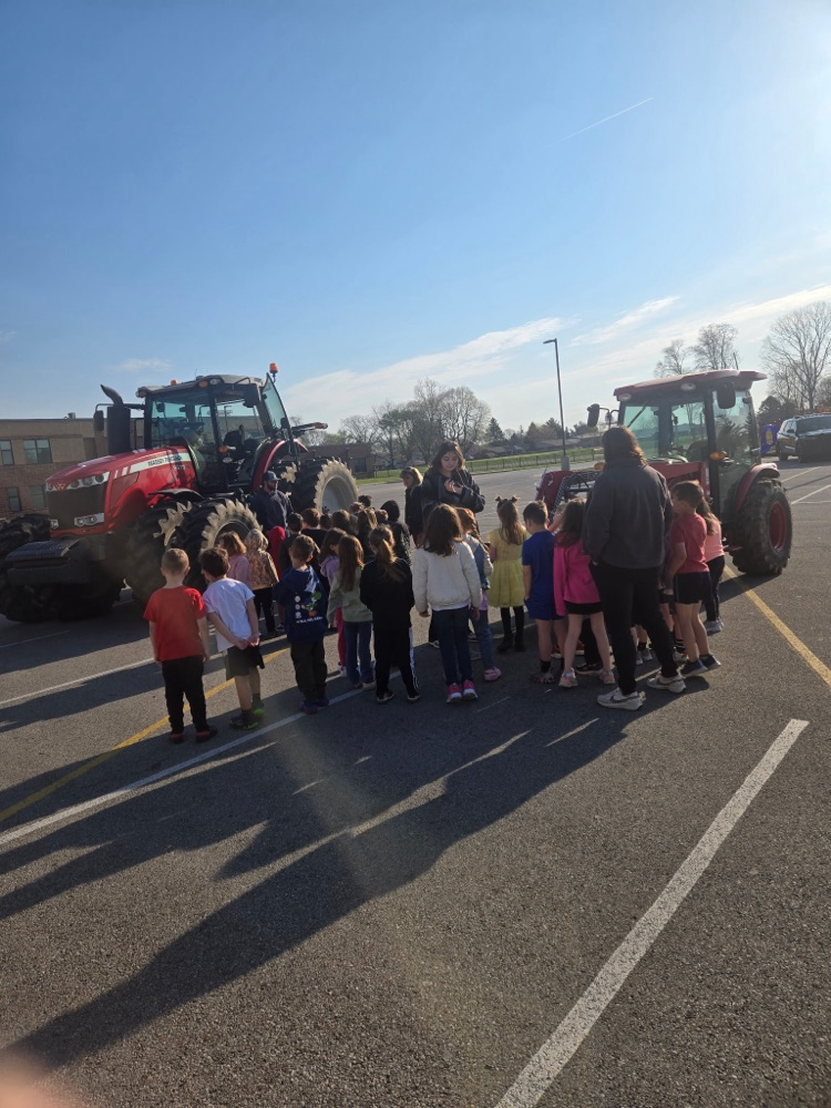 group of students listening to speaker with tractors in the background