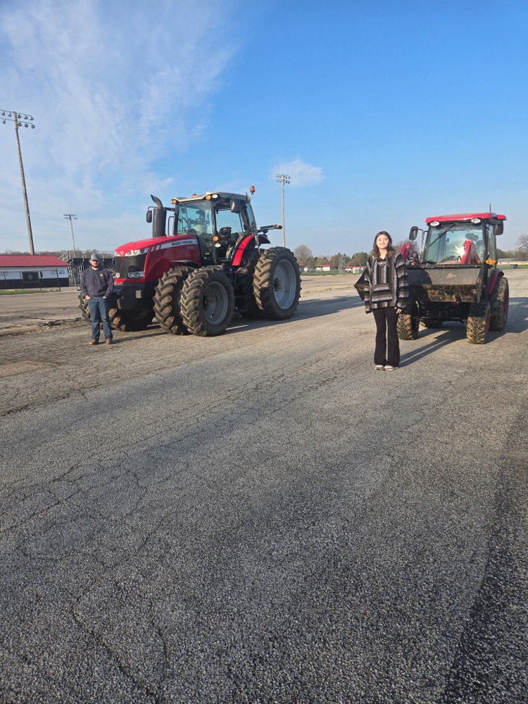 two students standing in front of 2 red tractors