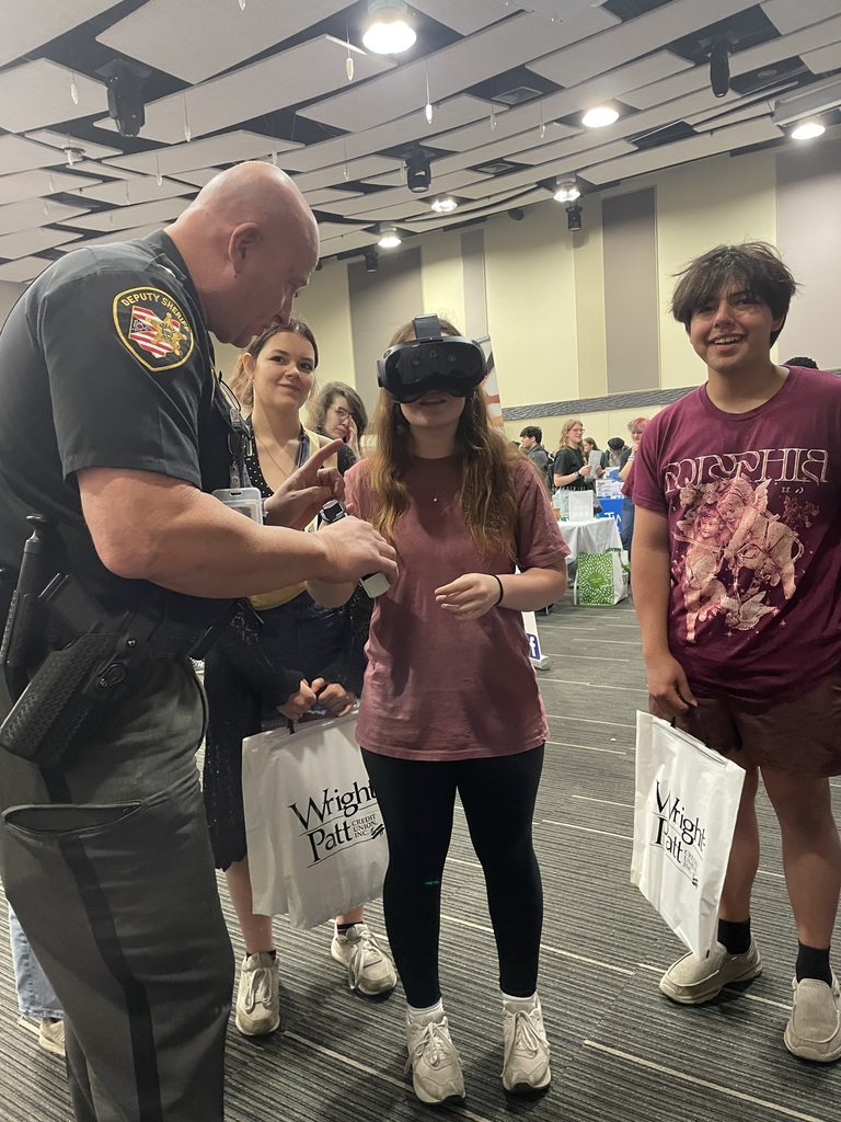 An officer shows a woman and a boy VR equipment inside a large room. The woman wears a black hat.