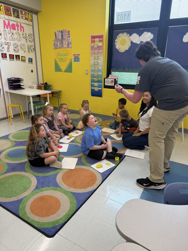 older student teacher presenting to younger students sitting on carpet