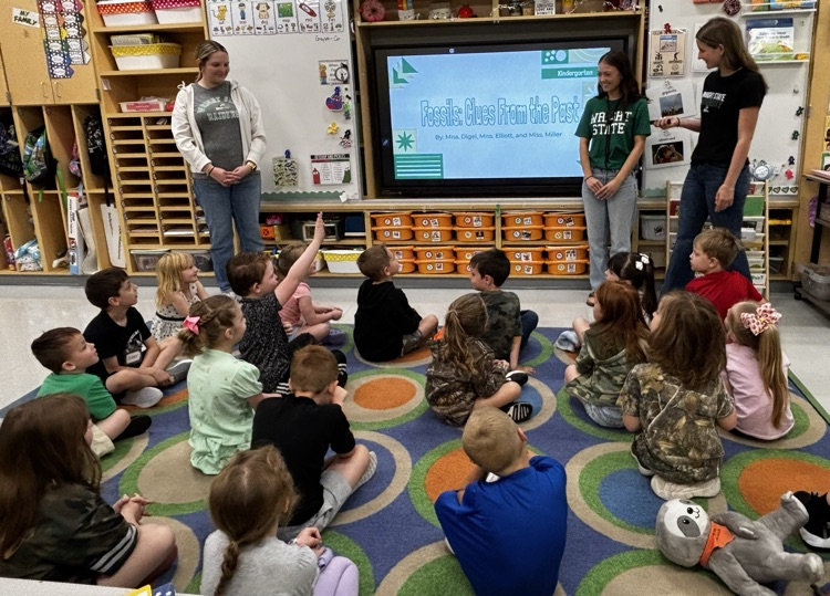 older student teacher presenting to younger students sitting on carpet