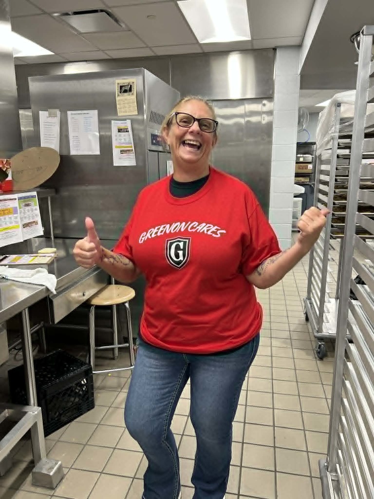 Person in a red shirt with "Greener Choices" printed on it, smiling and giving a thumbs up.