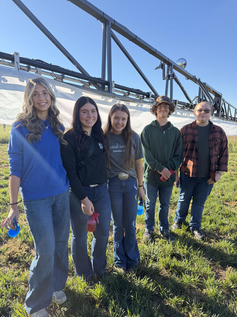 Five people stand in a field with a metal irrigation structure in the background.