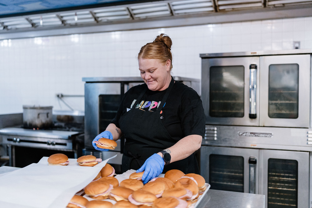 Woman placing sandwiches on a cooking tray in a kitchen