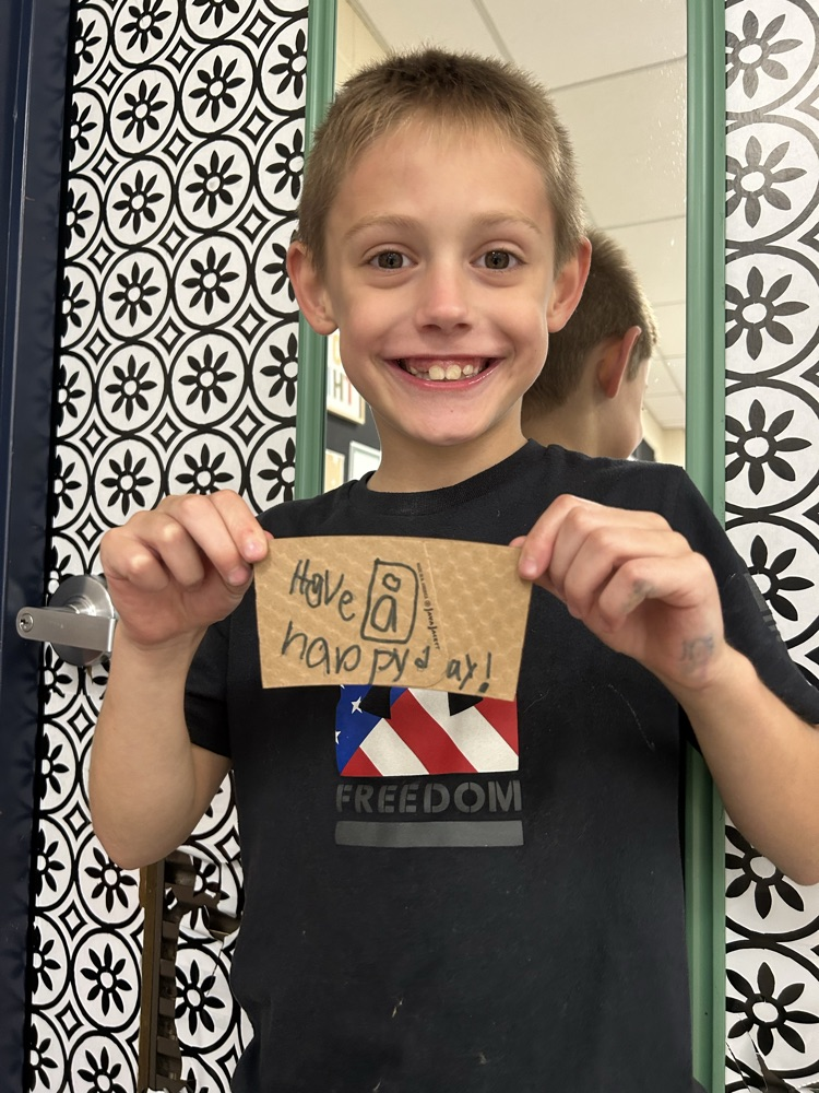 student smiling holding up a shine coffee sleeve they designed