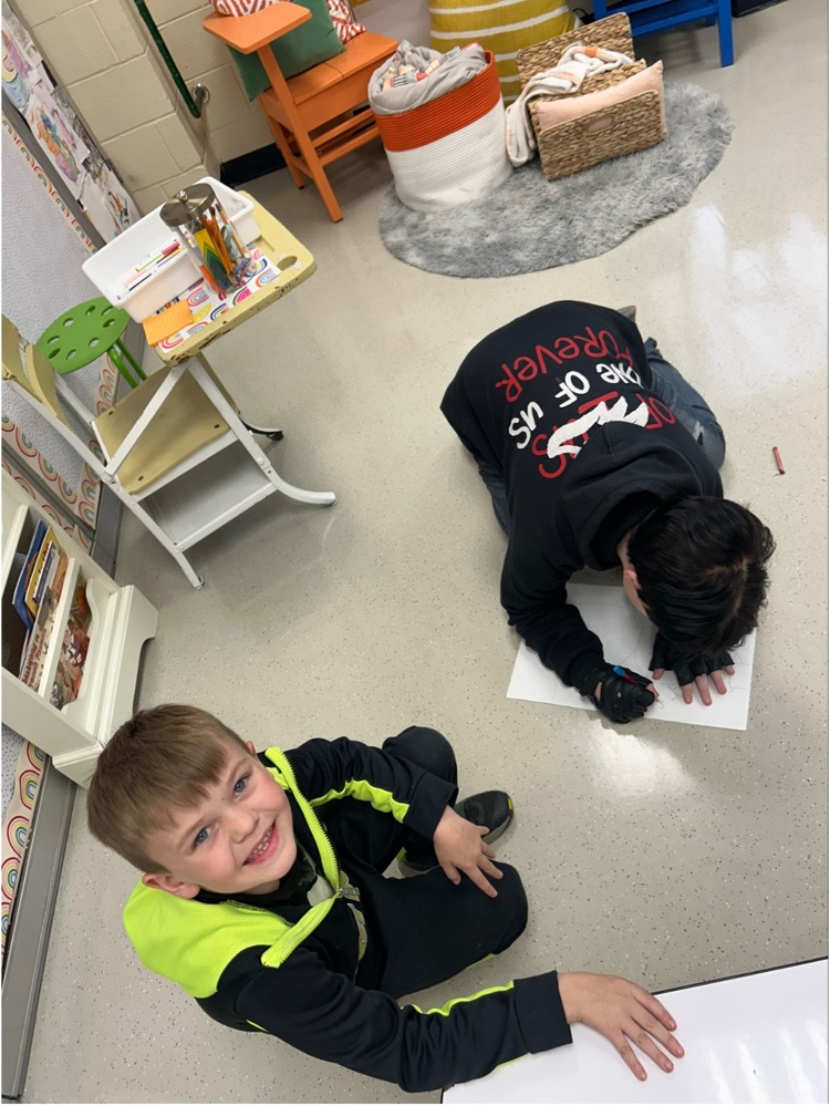 two male students are working on sketching a snowman, one student is drawing while one student smiles at the camera
