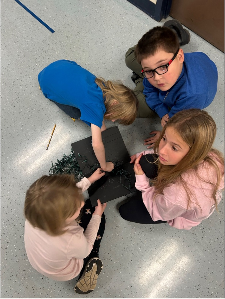 four students are working together to string lights into a mini black billboard