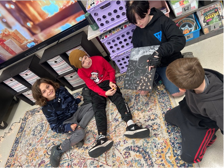 four students showcase their near complete light up snowman made out of a chalk sketch, and string lights