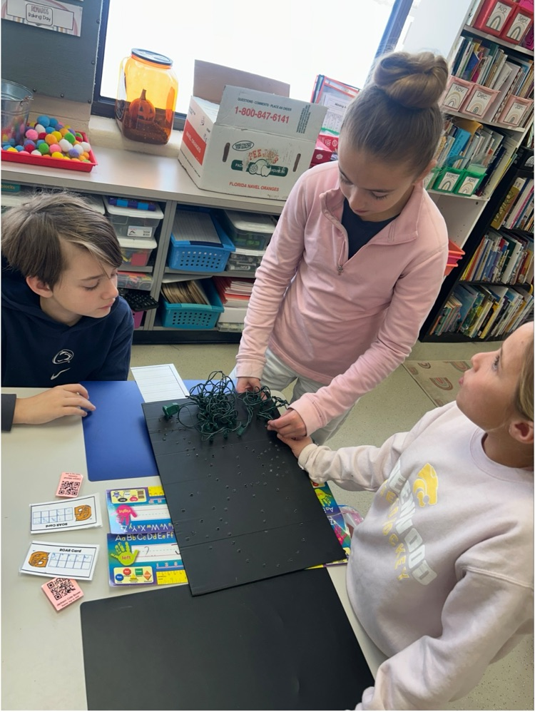 three students string lights into a black billboard