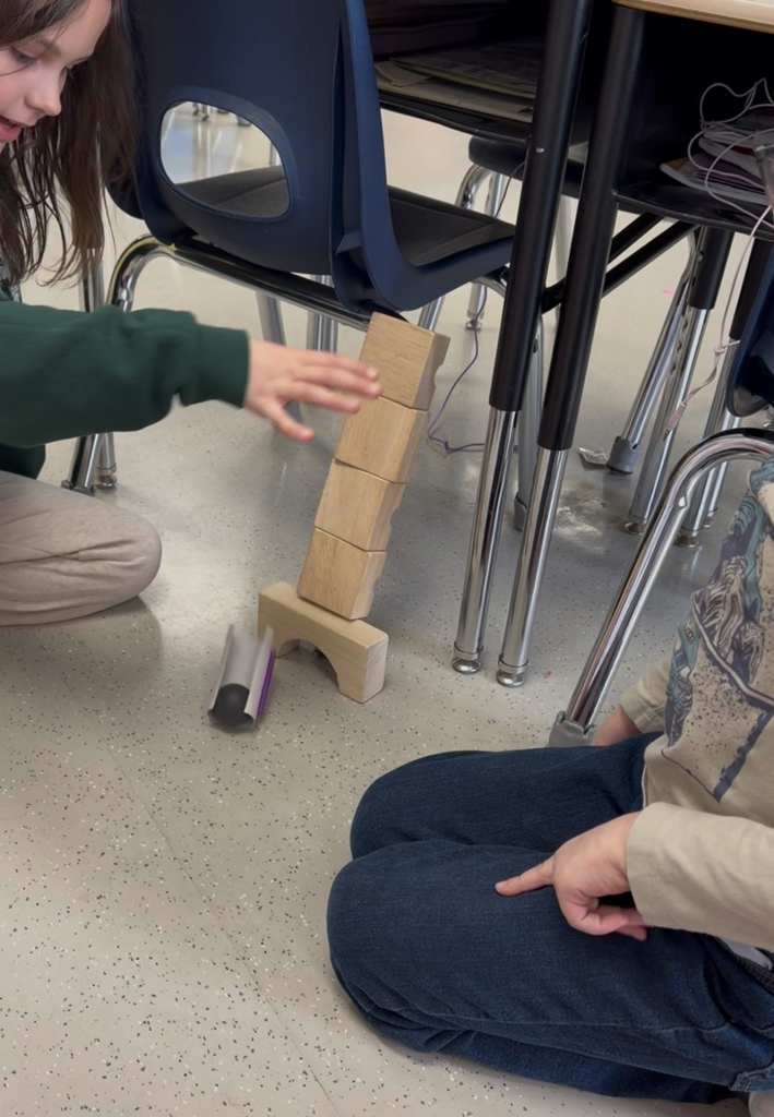 two students who are out of frame test their bobsleigh on a ramp they made out of blocks 