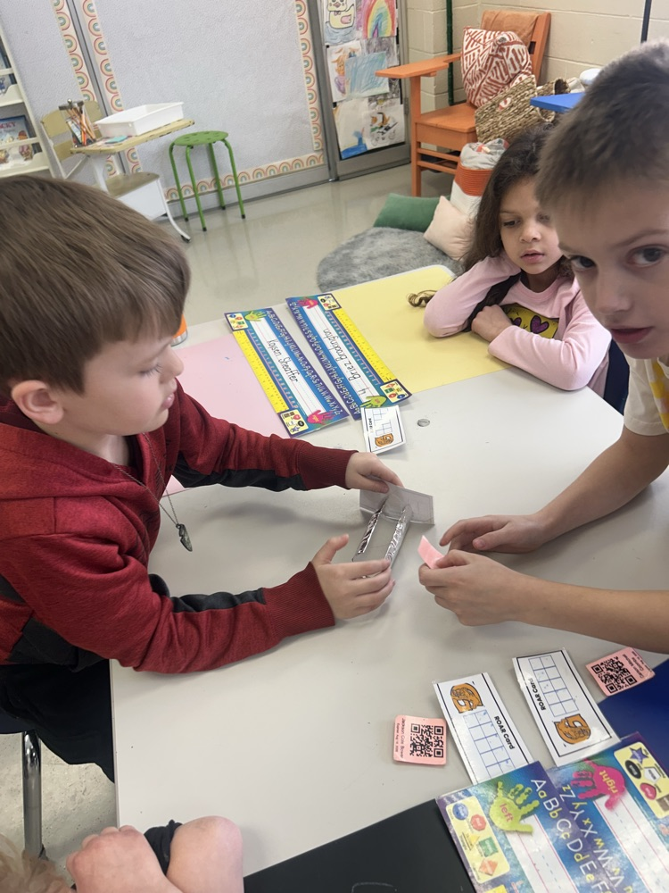 three students work together to build a bobsleigh out of a toilet paper roll, tinfoil, ping pong ball and a tooth pick 