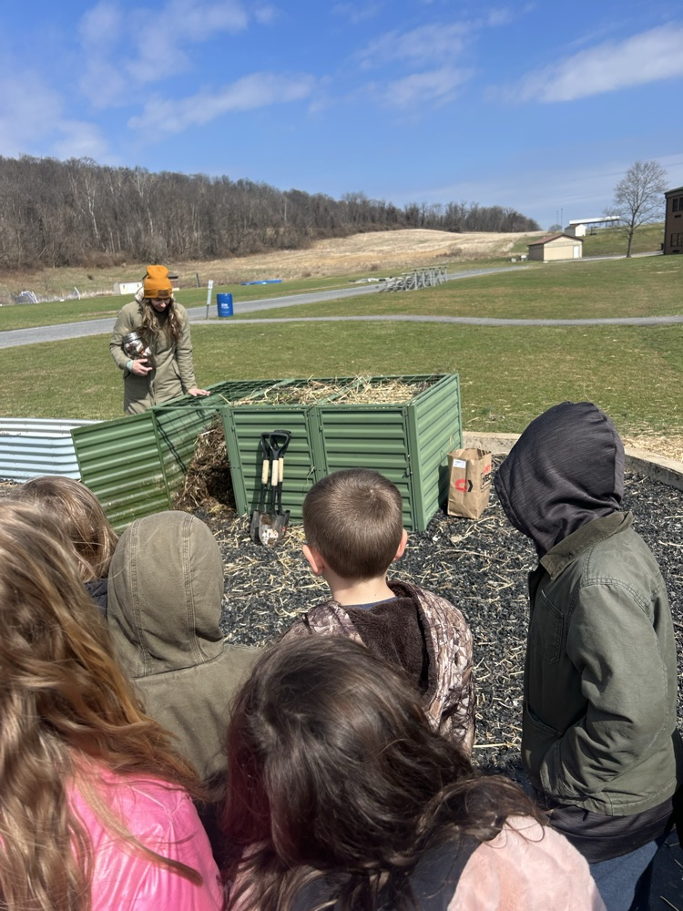 students gather around the outdoor compost bin to look at organic material that has turned into soil 