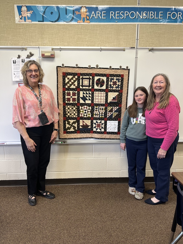 Mrs. Blair, Lori Amey, and her granddaughter, Emilie Nastasi, next to a handmade quilt. 