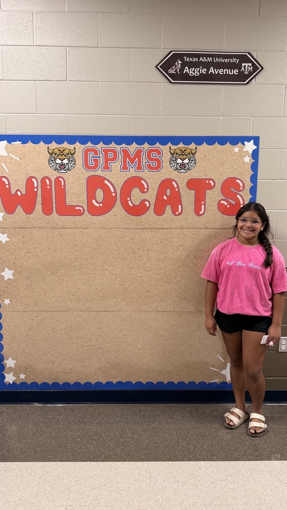 A young woman standing in front of a bulletin board with "GPMS Wildcats" text and school logo.