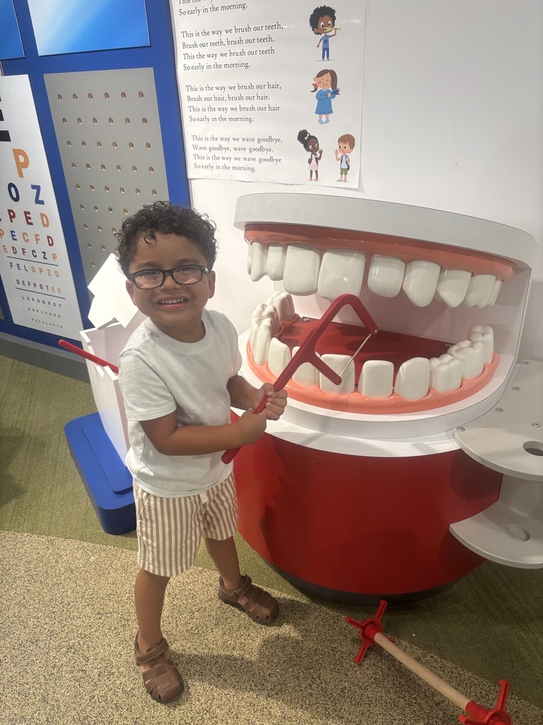 A young child smiling and posing next to a large dental model in a medical office.