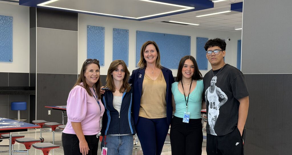 A group of five young people standing together in what appears to be an office or classroom setting, smiling at the camera.