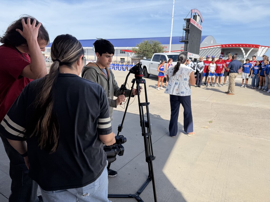 A group of people with cameras and tripods in front of a theme park entrance with a large sign.