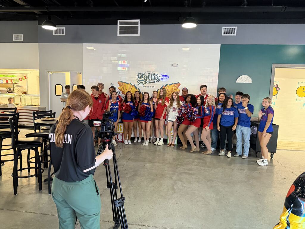 A group of people in colorful uniforms, standing in a large indoor space with seating, signage, and lighting fixtures.