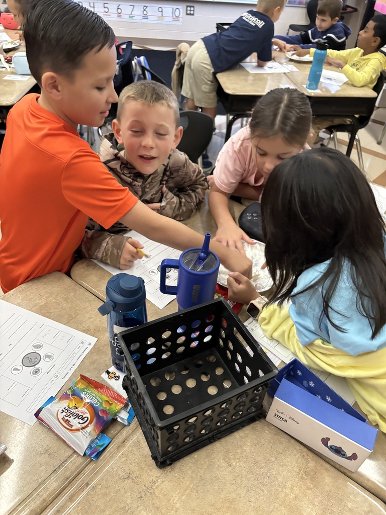 Young students collaborating on a project at a desk in a classroom, using various learning materials and tools.